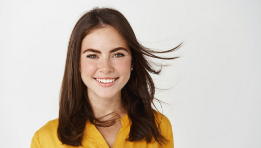 A woman with a cheerful expression, wearing a yellow blouse, smiling naturally at the camera in a well-lit portrait setting.